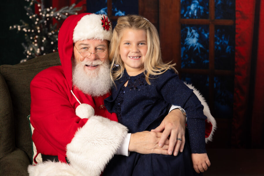 Girl in blue dress sitting on Santa's lap during a Santa photo session in Mebane, NC