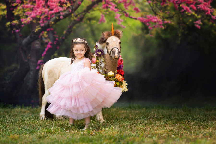 Girl twirling in her dress while standing by mini unicorn.