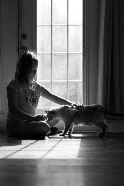 Portrait of a girl and cat sitting in the sunshine by a door.